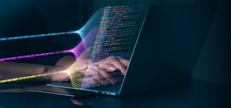 Pictorial representation of Donut malware. Image showing a person typing on a laptop with a graphic of colorful data streams flowing from the screen, symbolizing digital data transfer and technology.