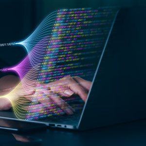 Pictorial representation of Airstalk malware. A person typing on a laptop with digital graphics of binary code and light beams emanating from the screen, representing data transfer or cyber activity.
