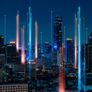 Pictorial representation of an authentication coercion attack. Panoramic view of a city skyline at night, featuring vibrant light beams from skyscrapers and a deep blue sky.