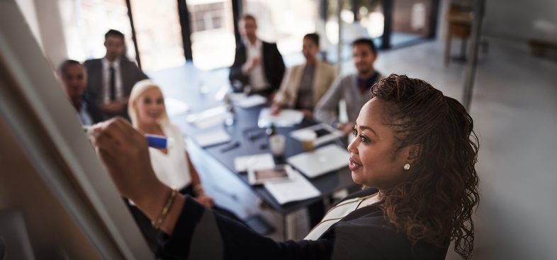 Pictorial representation of a group of individuals discussing an idea with a whiteboard.