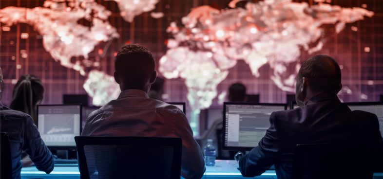 Pictorial representation of security risks in AI models. A group of people is seated at computer workstations in a dimly lit room, facing a large screen displaying a world map with data visualizations.