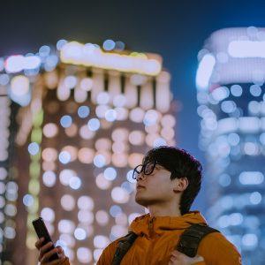 Pictoral representation of a man holding a cellphone with a bokeh skyline in the background.