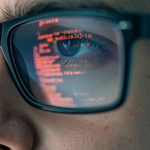 Pictorial representation of WebAuthn. A person wearing glasses with computer code reflected in the lenses. The focus is on the eye, and the code is clear and detailed.