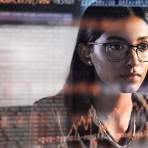 Pictorial representation of a woman in glasses viewing a reflection of a monitor screen. The reflection features multicolored numbers, arrows, and graphs.