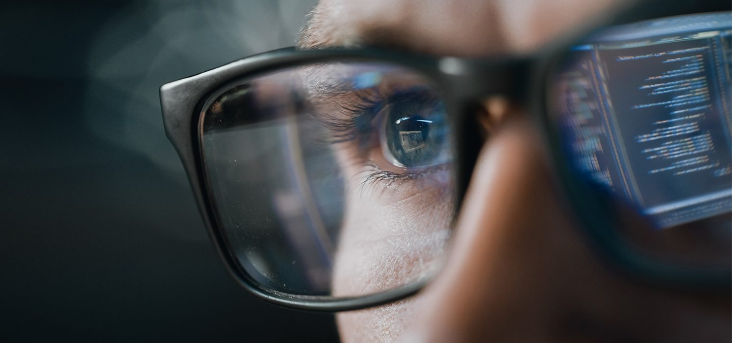 Pictorial representation of post-exploitation identity misuse in SPIFFE/SPIRE. Close-up of a person wearing glasses, with computer code reflected in the lenses.