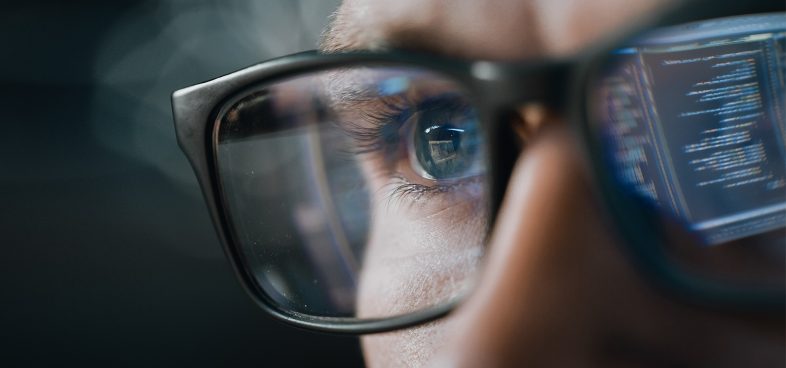 Pictorial representation of post-exploitation identity misuse in SPIFFE/SPIRE. Close-up of a person wearing glasses, with computer code reflected in the lenses.